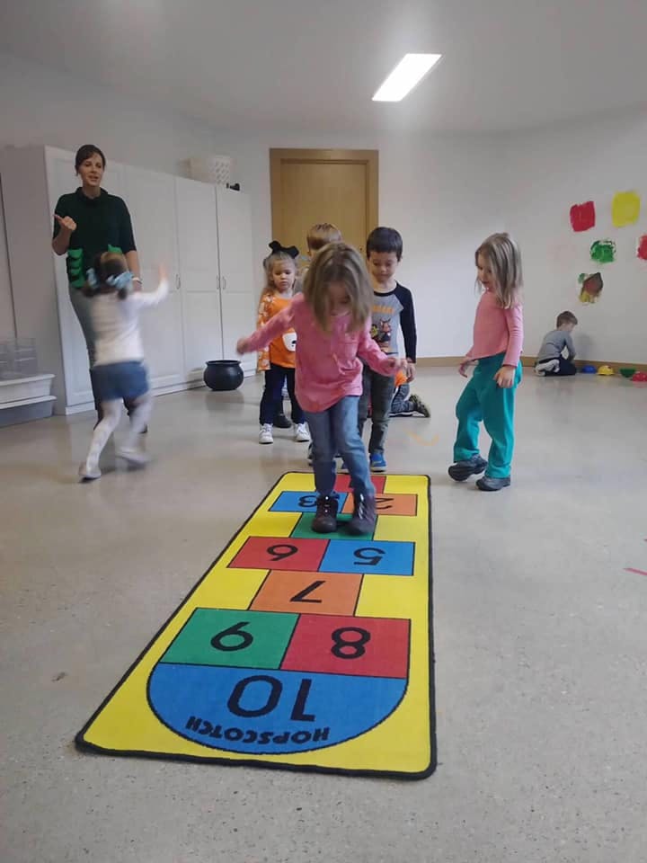 Children playing hopscotch on a colorful mat in a room