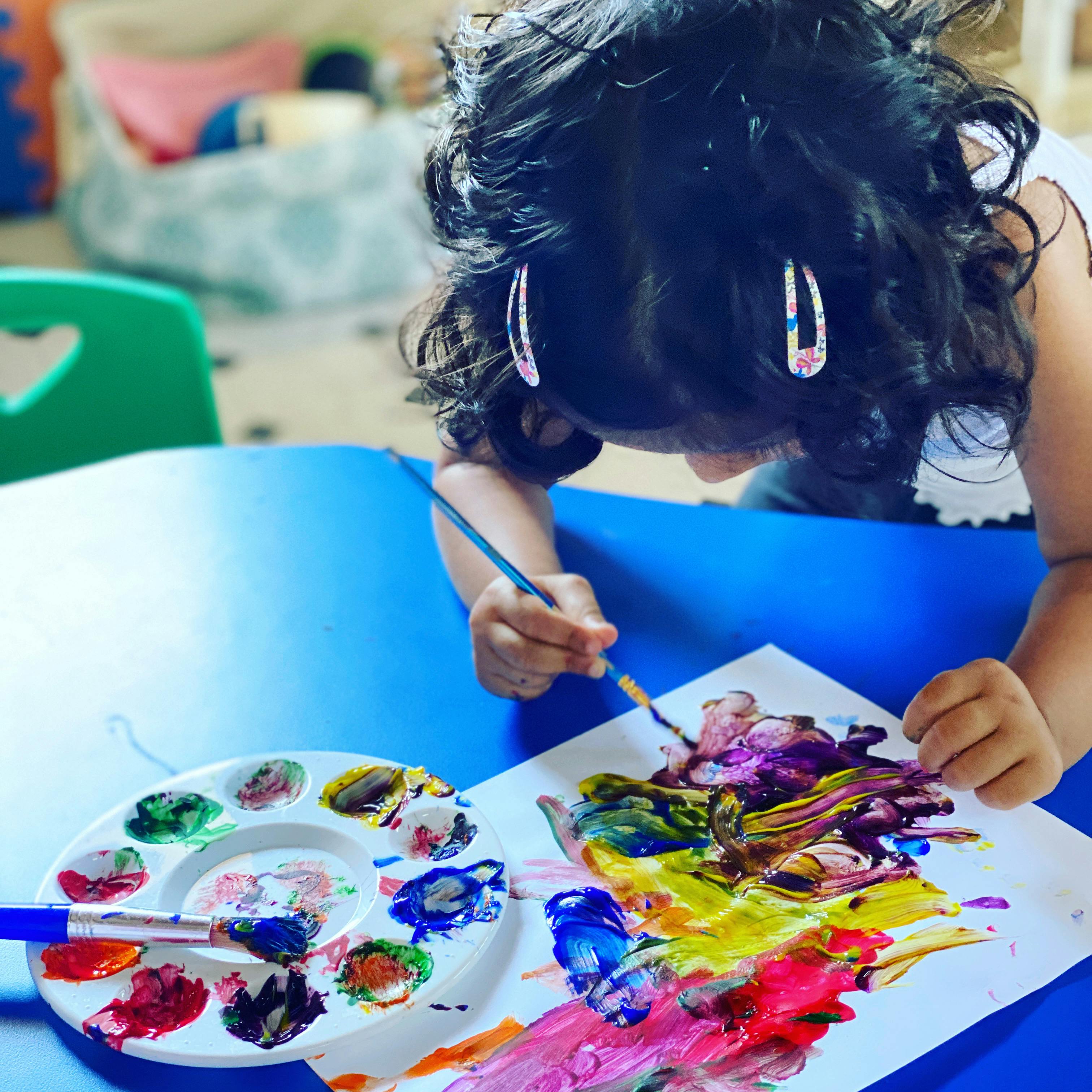 Child painting on paper with a brush and palette