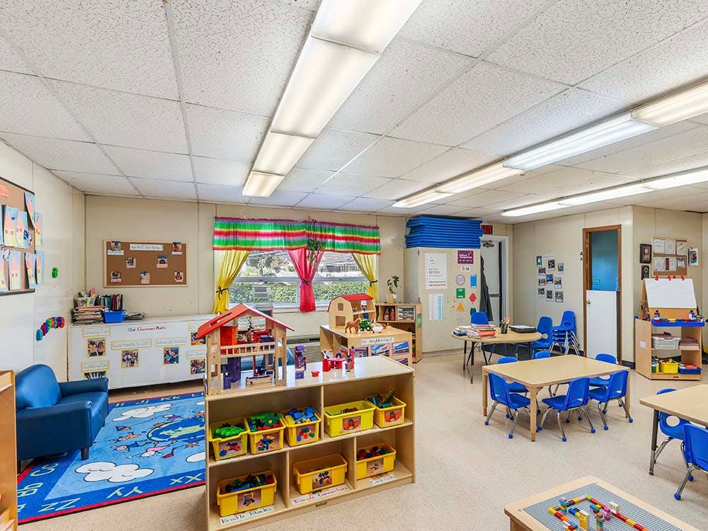 Classroom with small tables and chairs, toys, and child artwork on walls