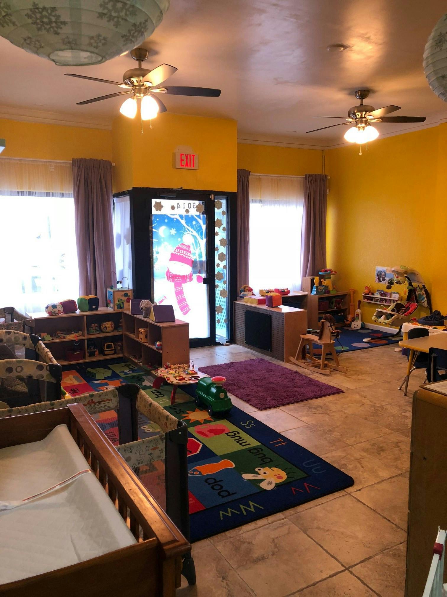 Daycare room with cribs, play mats, and shelves