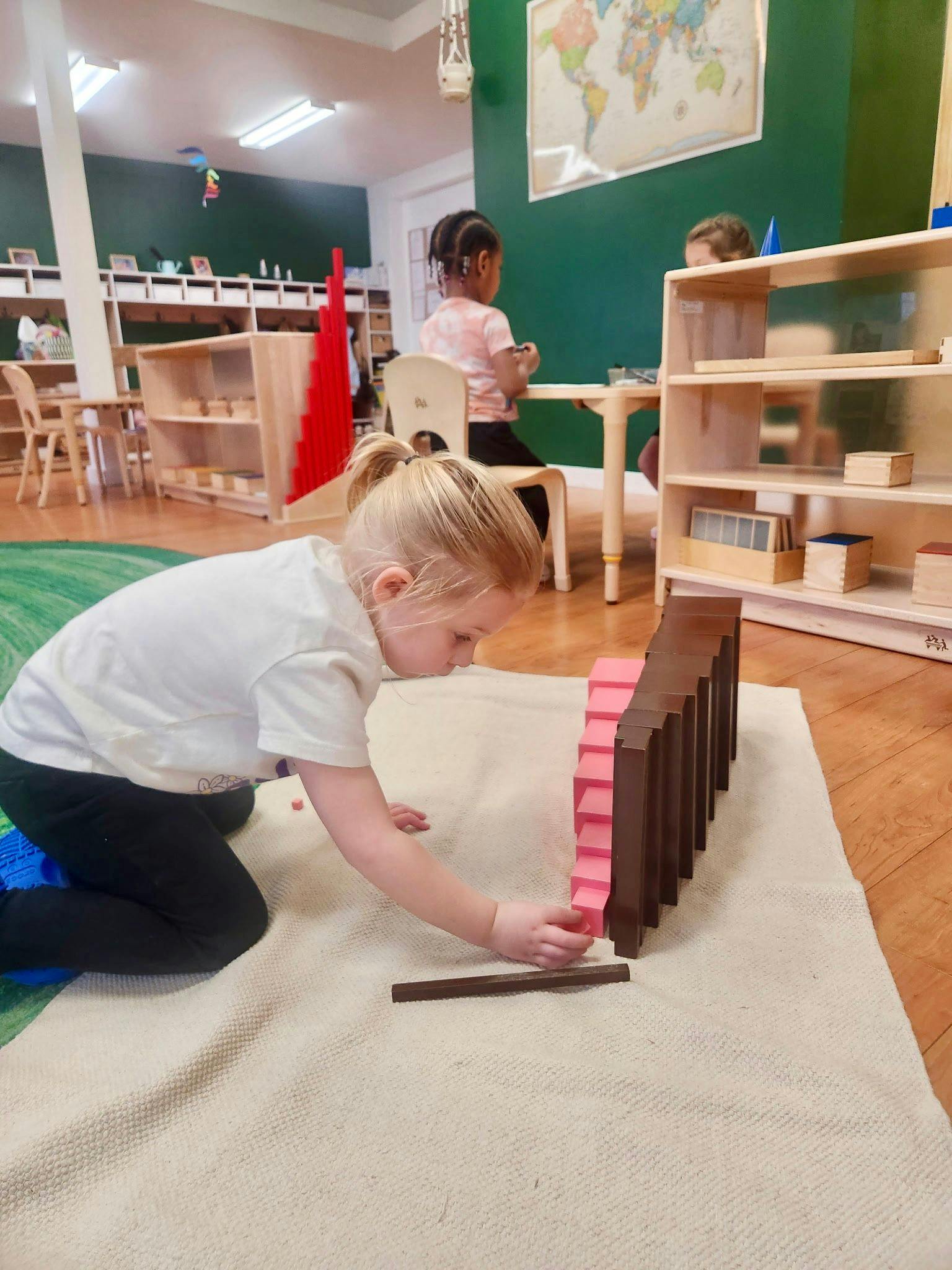 Child kneeling on a rug, placing a pink block next to a row of brown blocks