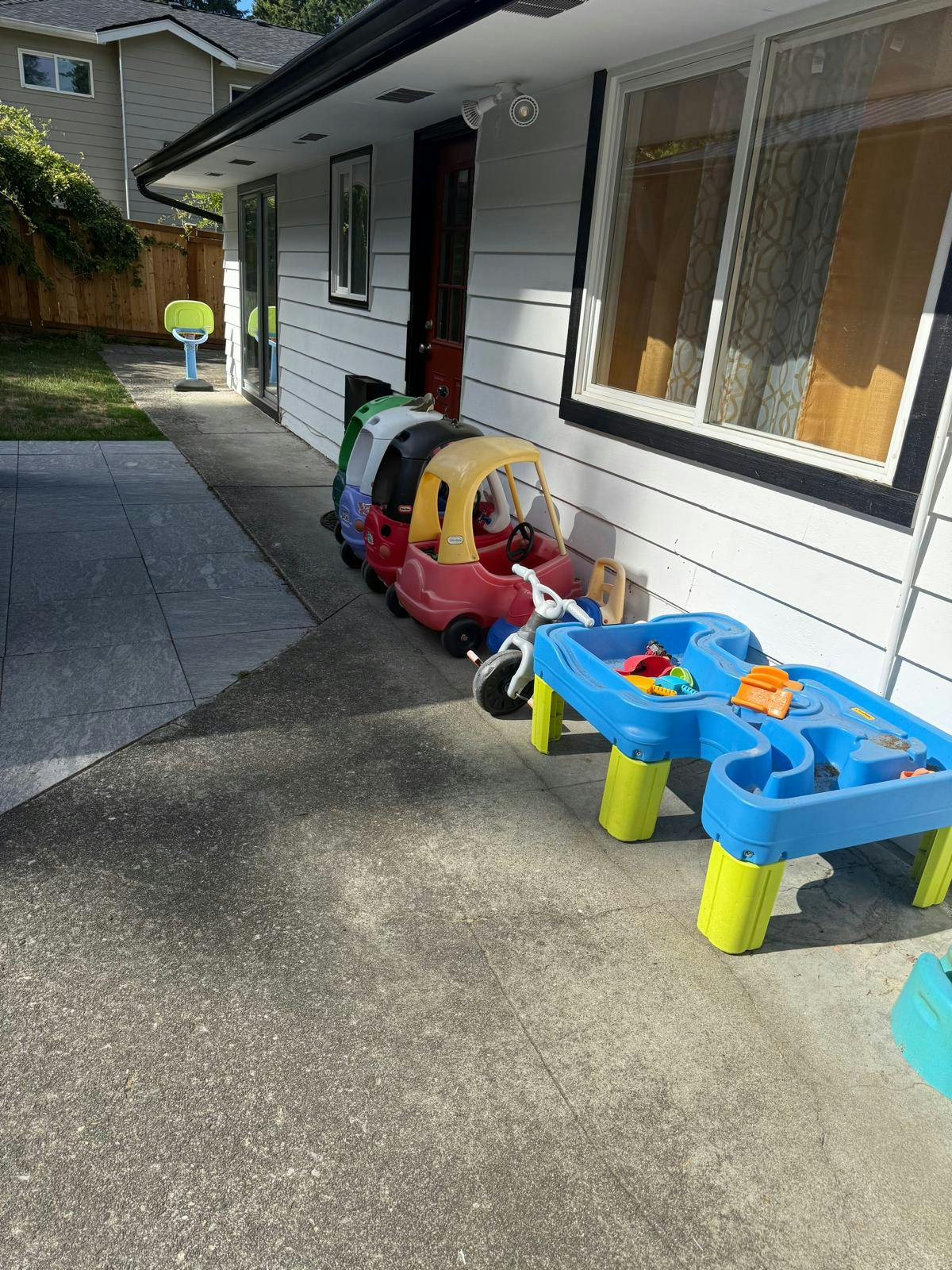 Children's toys lined up against a house, including ride-on cars and a water table