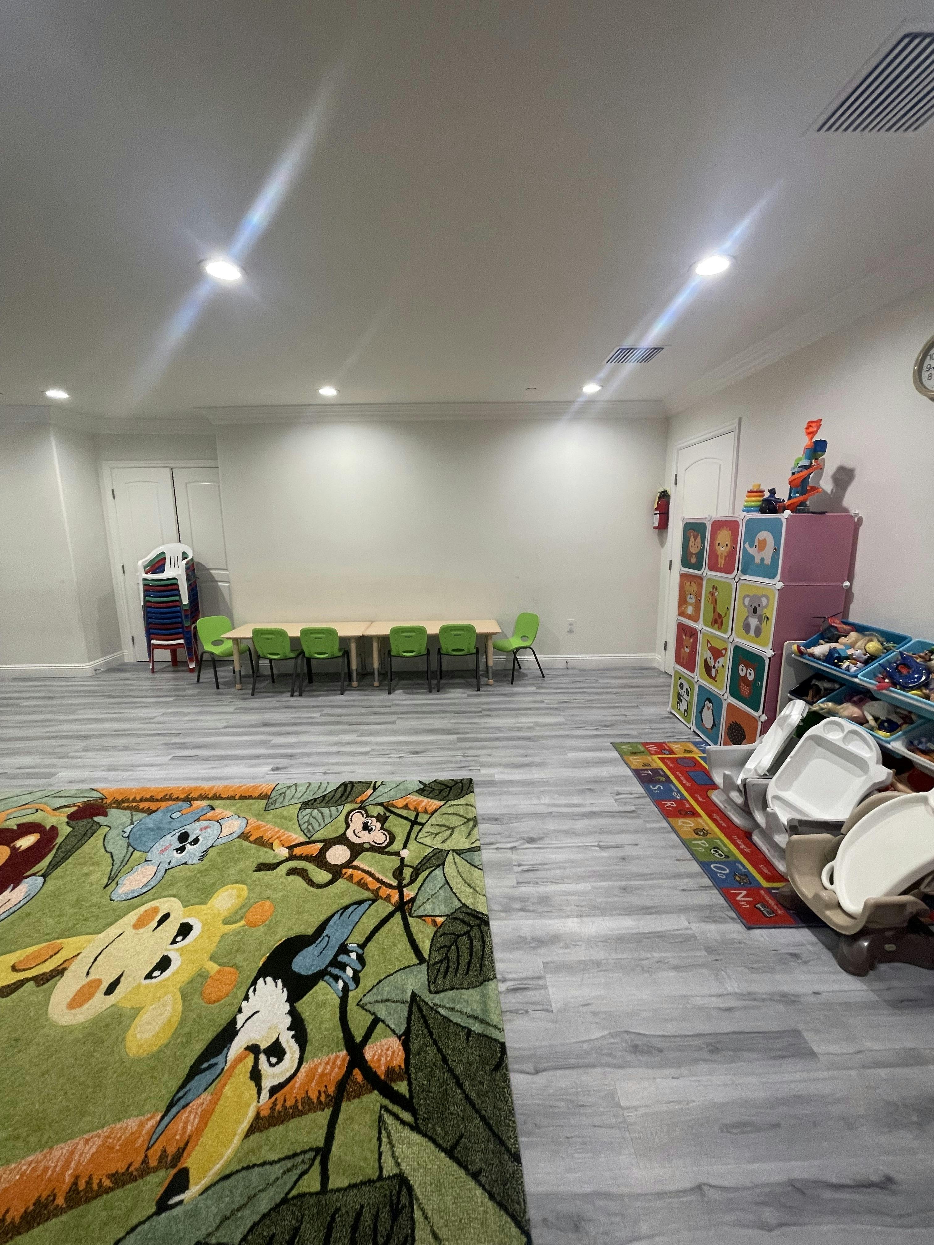 Playroom with a long table and green chairs, colorful rug, and storage shelves