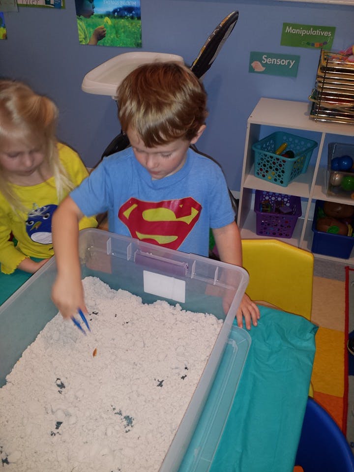Child playing with sand in a bin with a tool