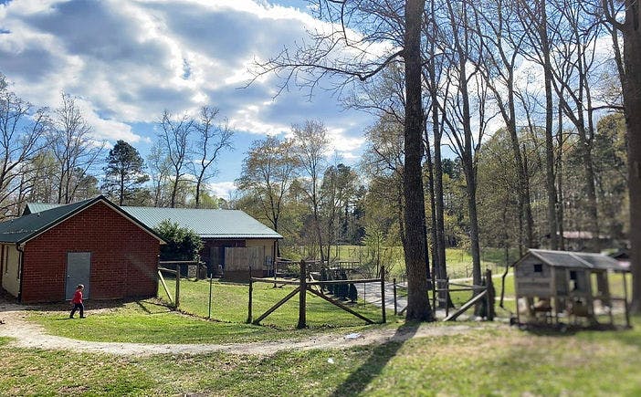 Child walking past a red barn with a fence and trees