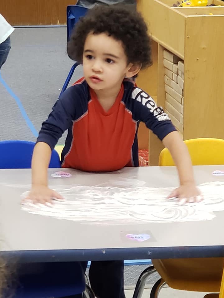 Child with curly hair pressing hands into white powder on a table
