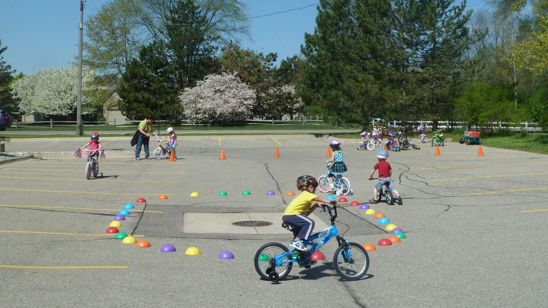 Children riding bicycles in a paved area with colorful cones