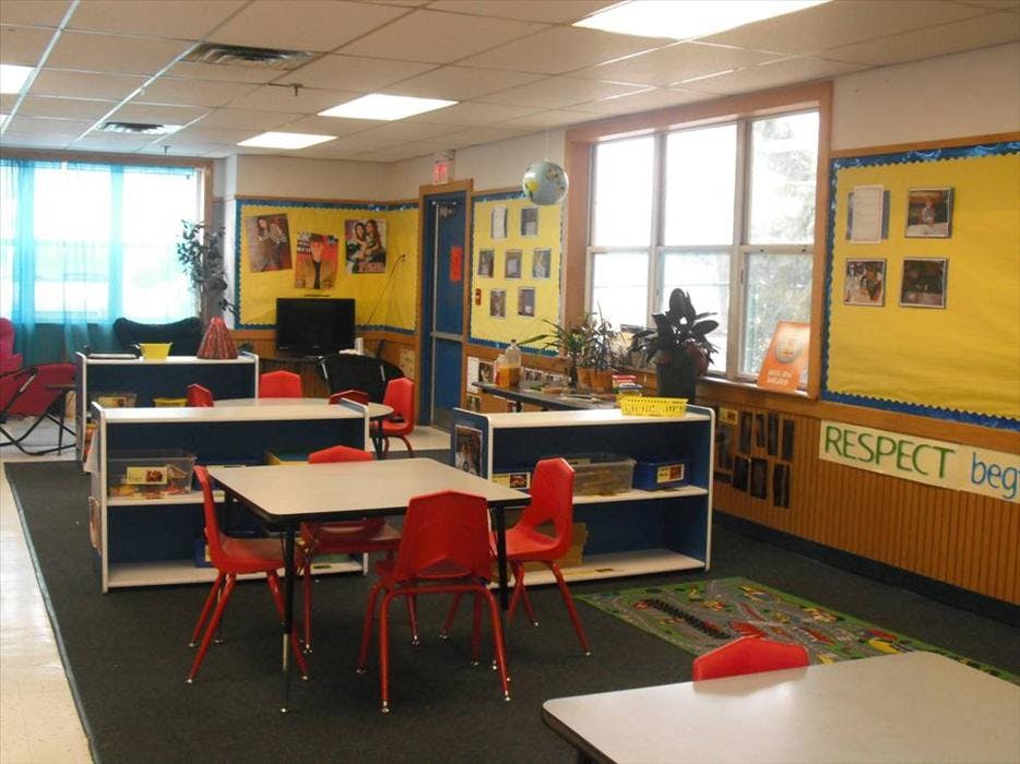 Empty classroom with small tables, red chairs, and yellow bulletin boards