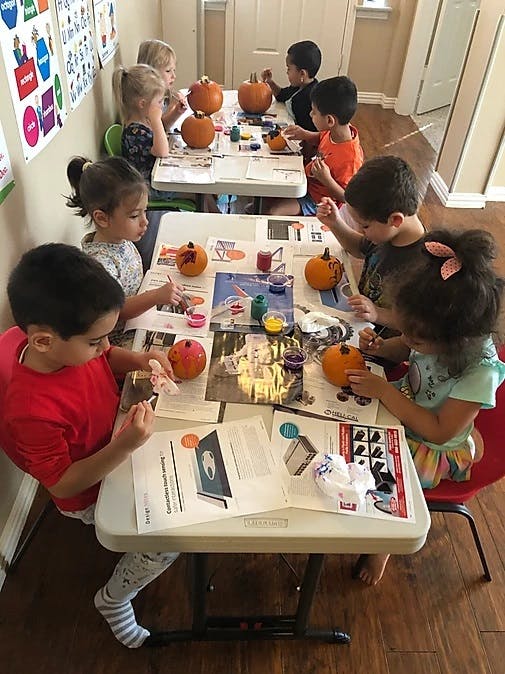 Children painting pumpkins at tables in a classroom