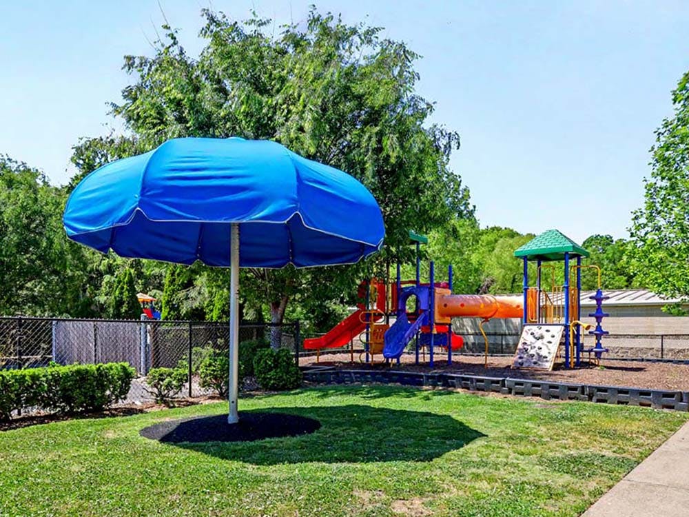 A blue umbrella in a grassy area with a playground structure