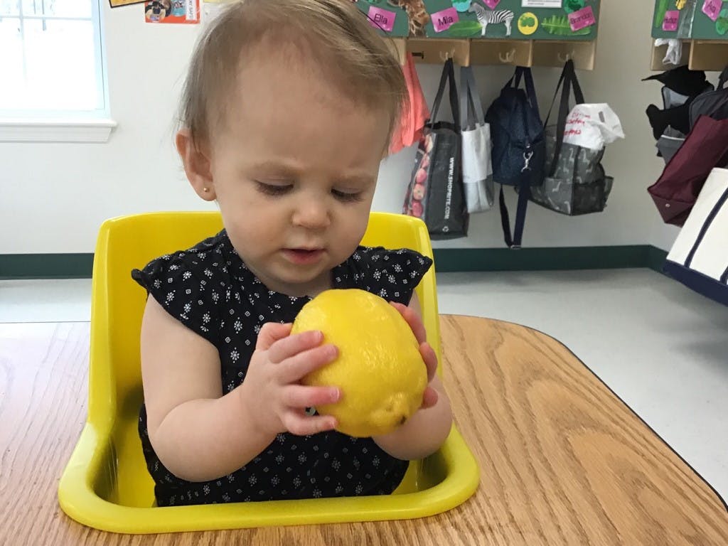 Child in a yellow chair holding a lemon