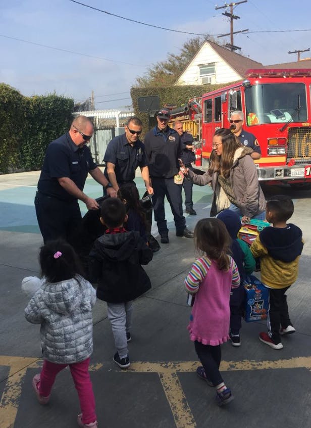 Firefighters interacting with children and an adult near a fire truck