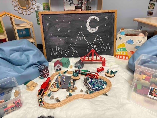 Toy train tracks with buildings and a chalkboard mountain scene in a classroom