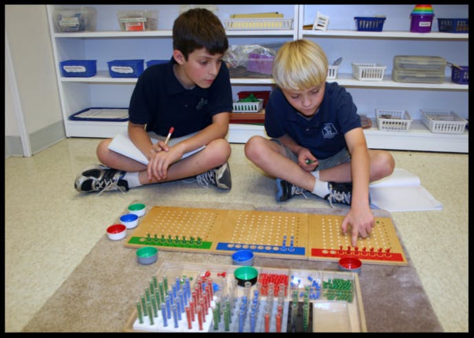 Two children sitting on the floor working with a learning board