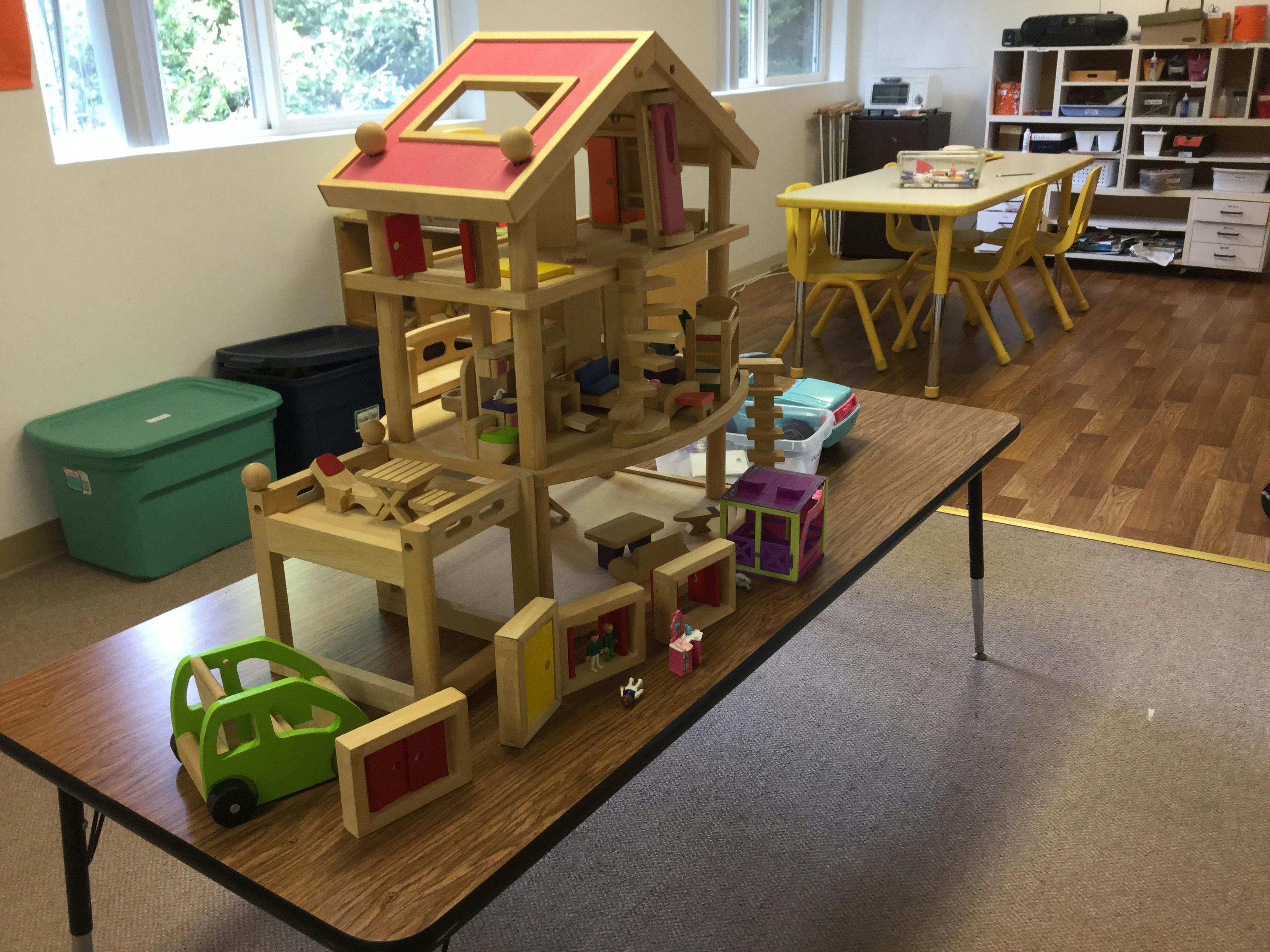 Wooden dollhouse and toy car on a table in a classroom