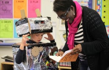 Child in robot costume with adult looking at book in classroom