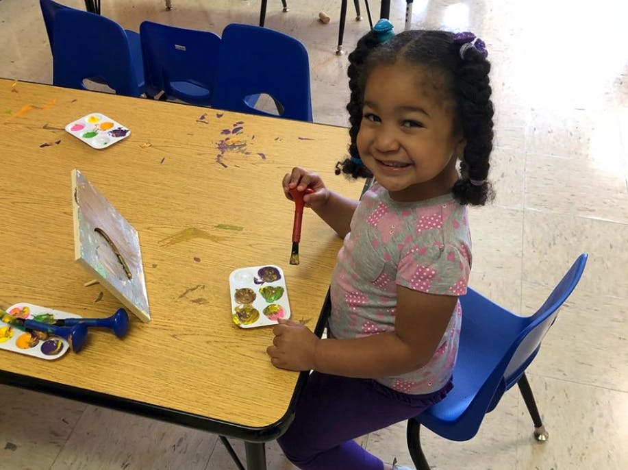 Child painting at a table with a paintbrush and paint palette