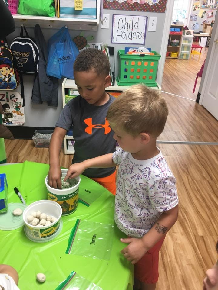 Two children playing with small objects in containers at a table