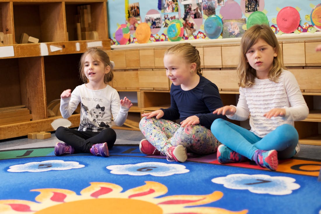 Three children sitting on a rug in a classroom