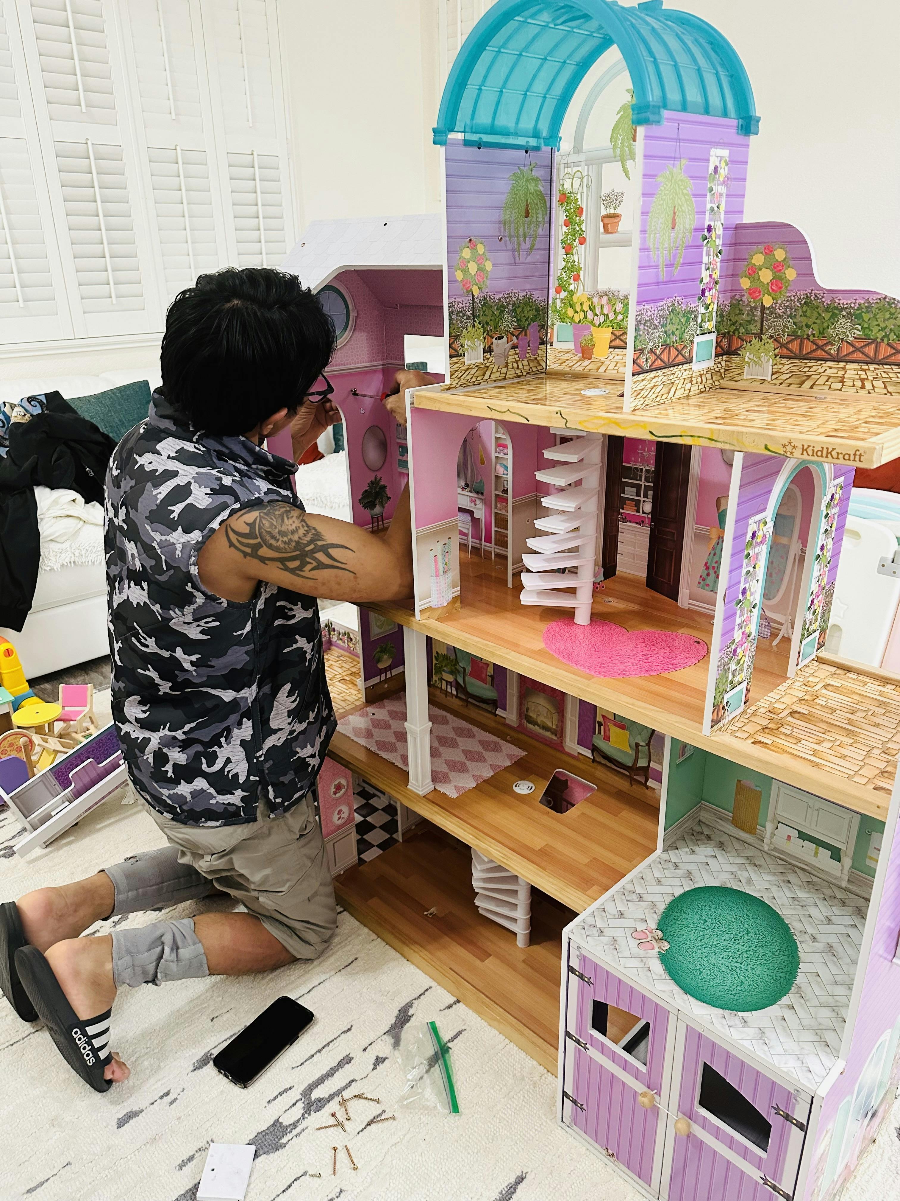 Person assembling a multi-story dollhouse on the floor