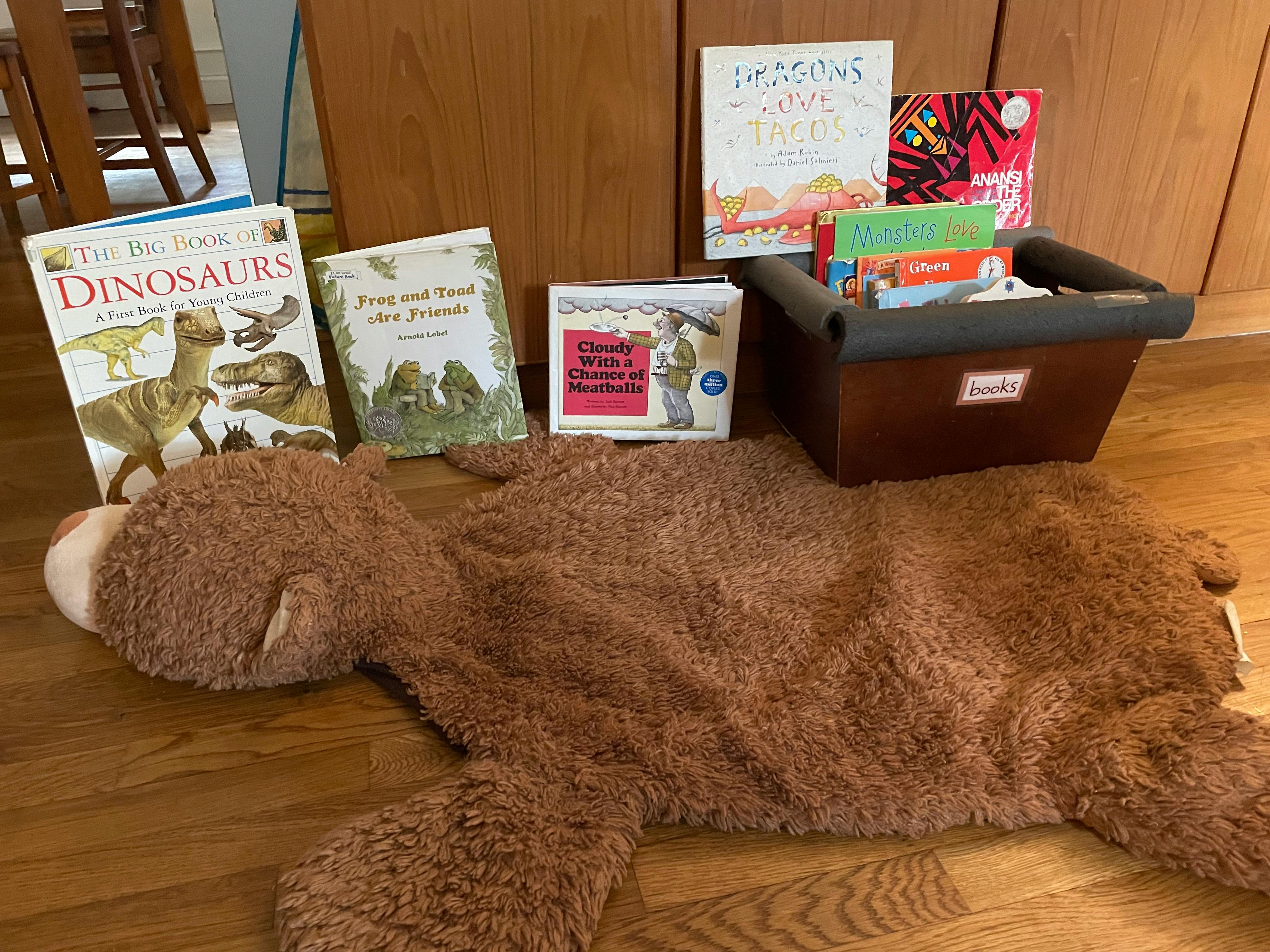 Large brown stuffed animal on floor with children's books and book bin