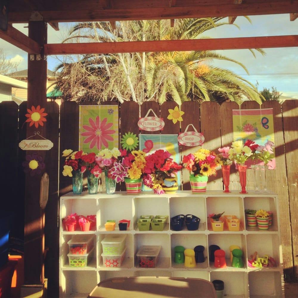 Shelves with colorful items and flowers in front of a wooden fence