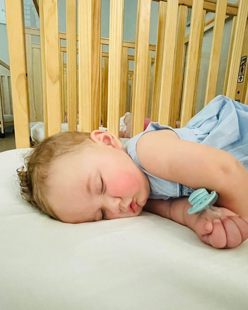 Child sleeping in a crib with a pacifier on their wrist