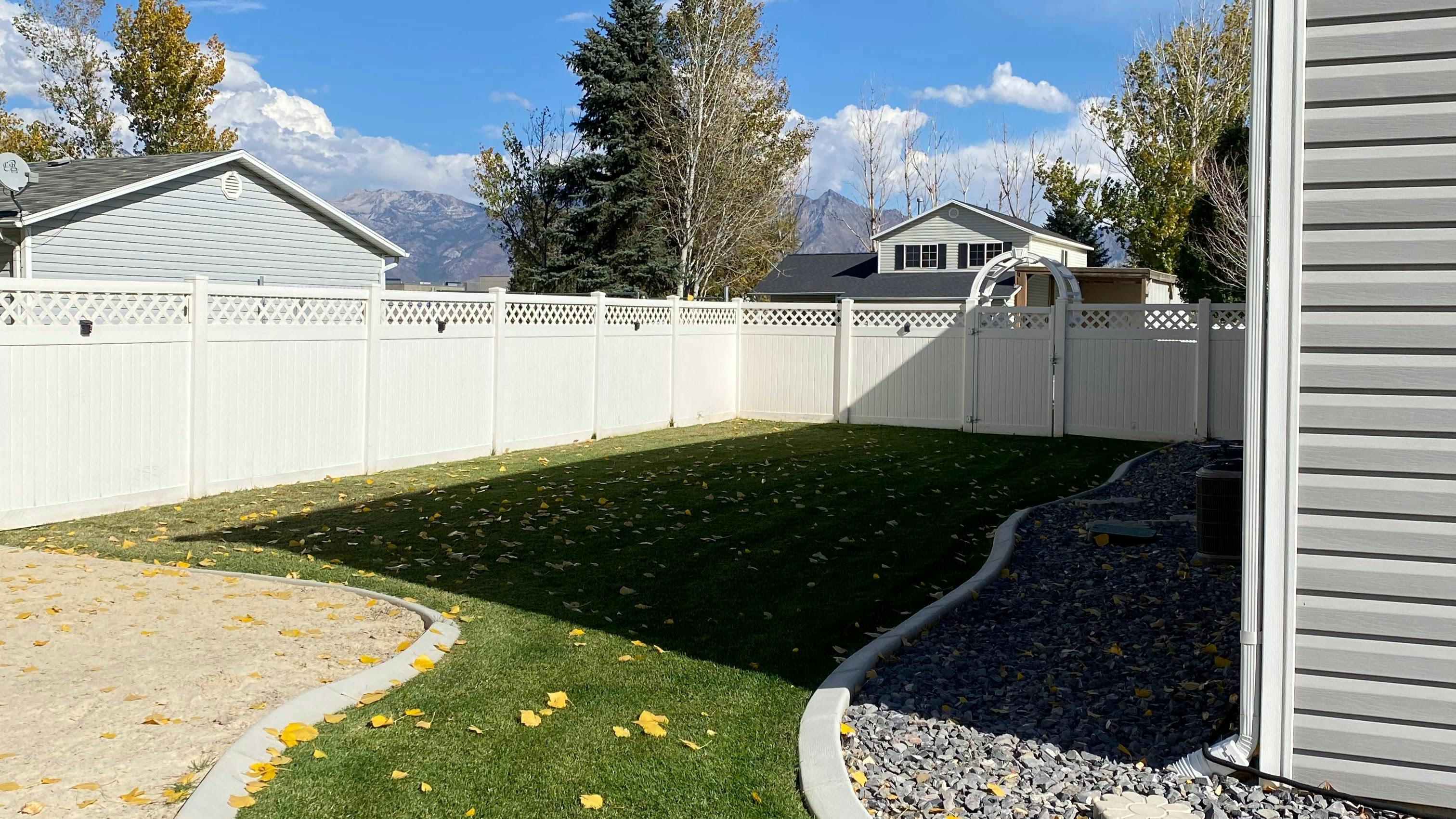 Backyard with white fence, green grass, and gravel path