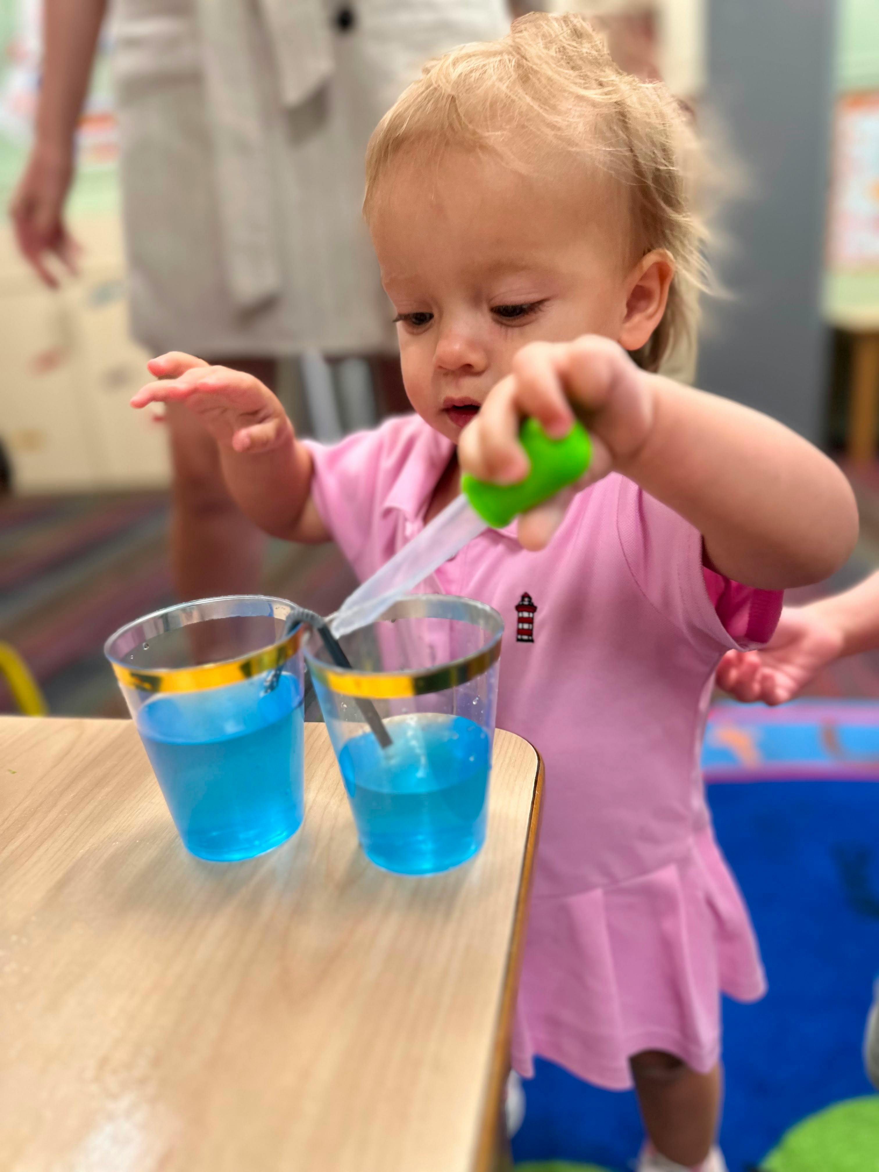Child using a dropper to transfer blue liquid between two plastic cups