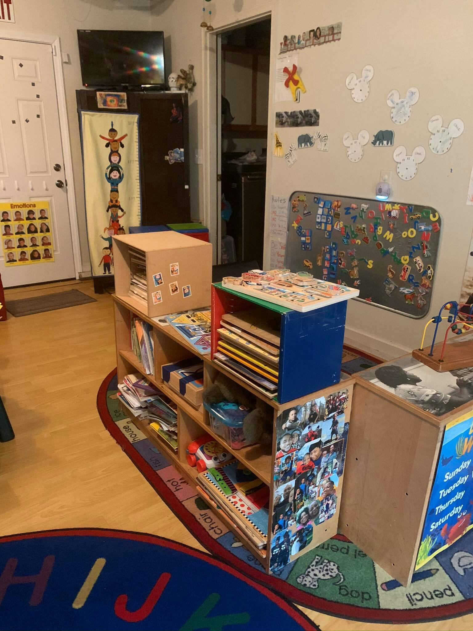 Classroom with shelves of books and toys, a whiteboard, and a rug with letters