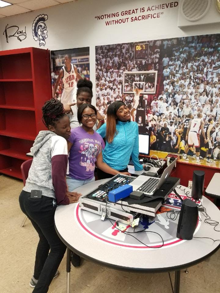 Four teens standing around a table with a laptop and sound equipment