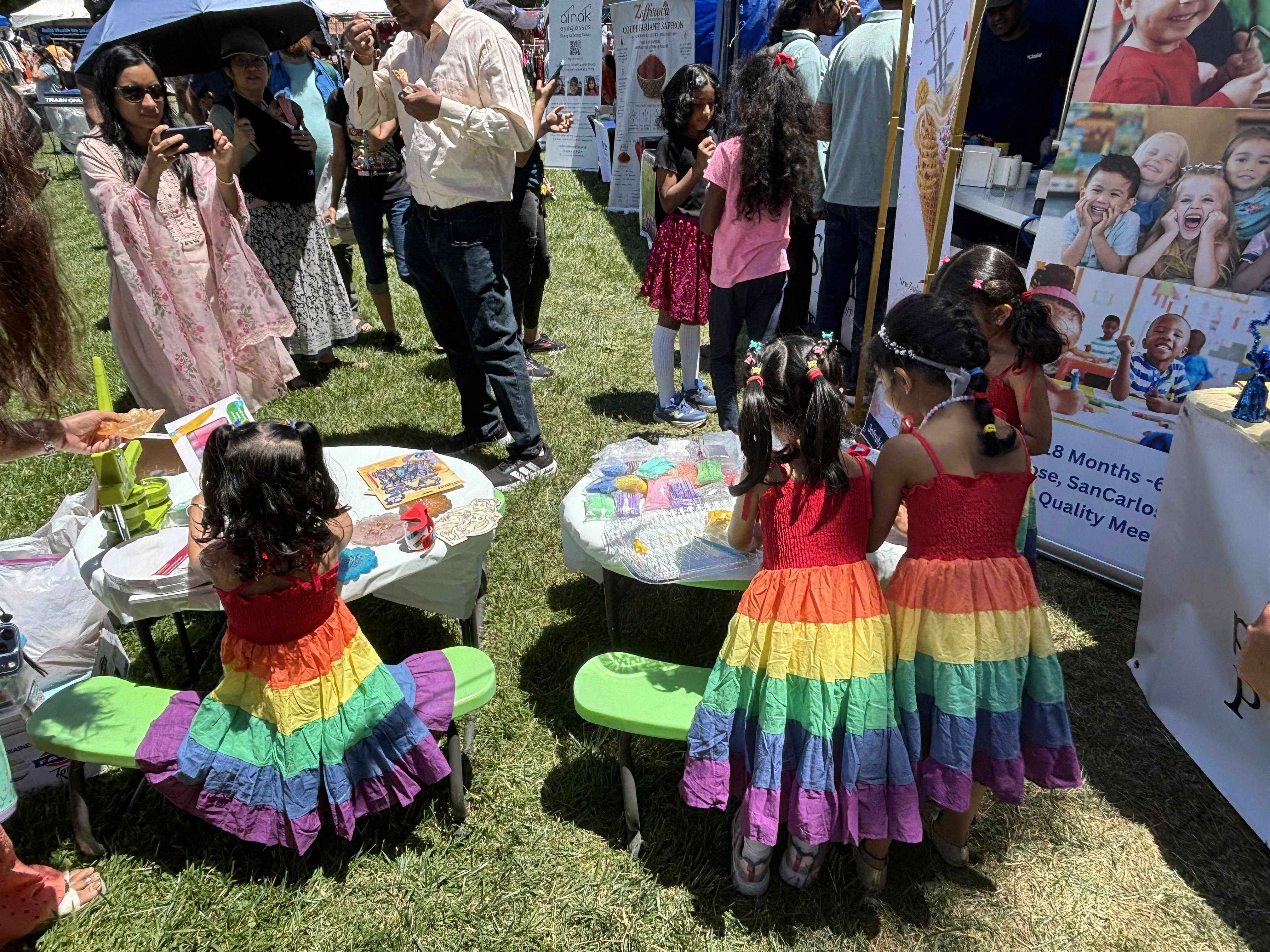 Children in rainbow dresses crafting at small tables during an outdoor event