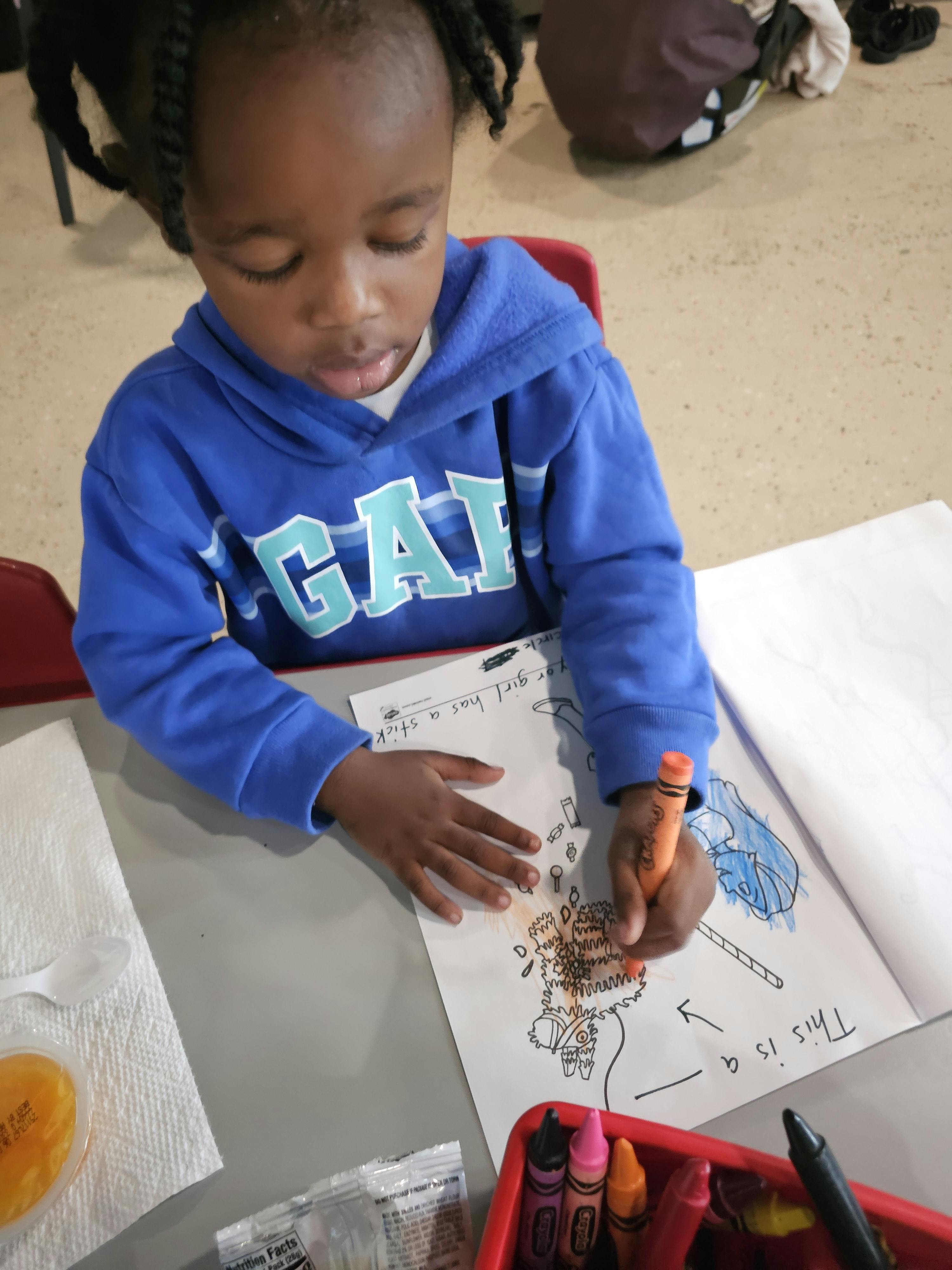 Child in blue hoodie coloring a drawing with a crayon