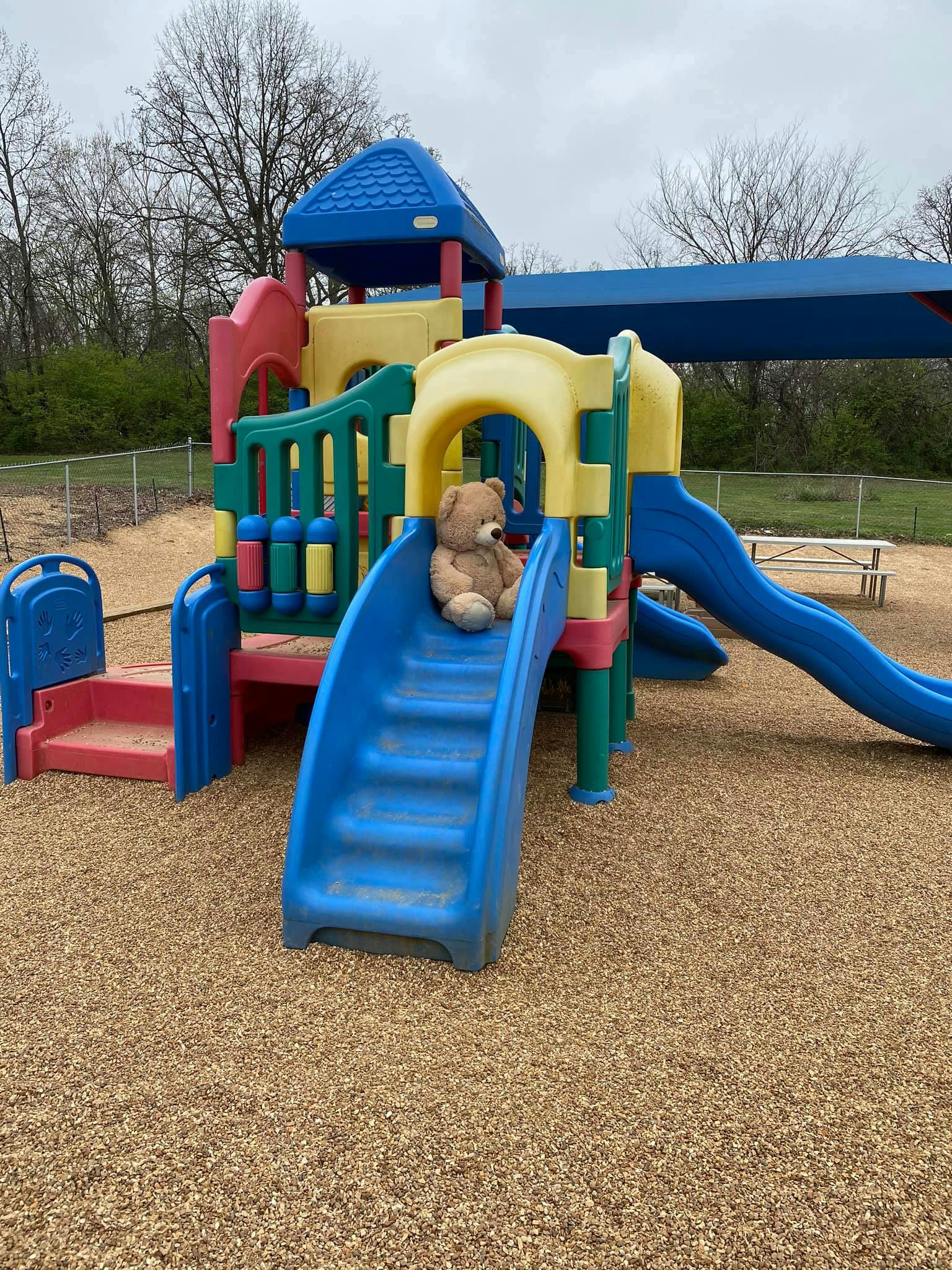 Teddy bear sitting on a blue slide on a playground