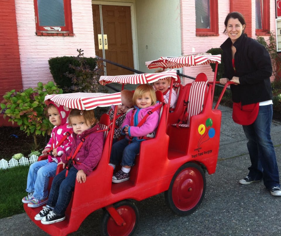 Person pushing multiple children in a red multi-seat stroller