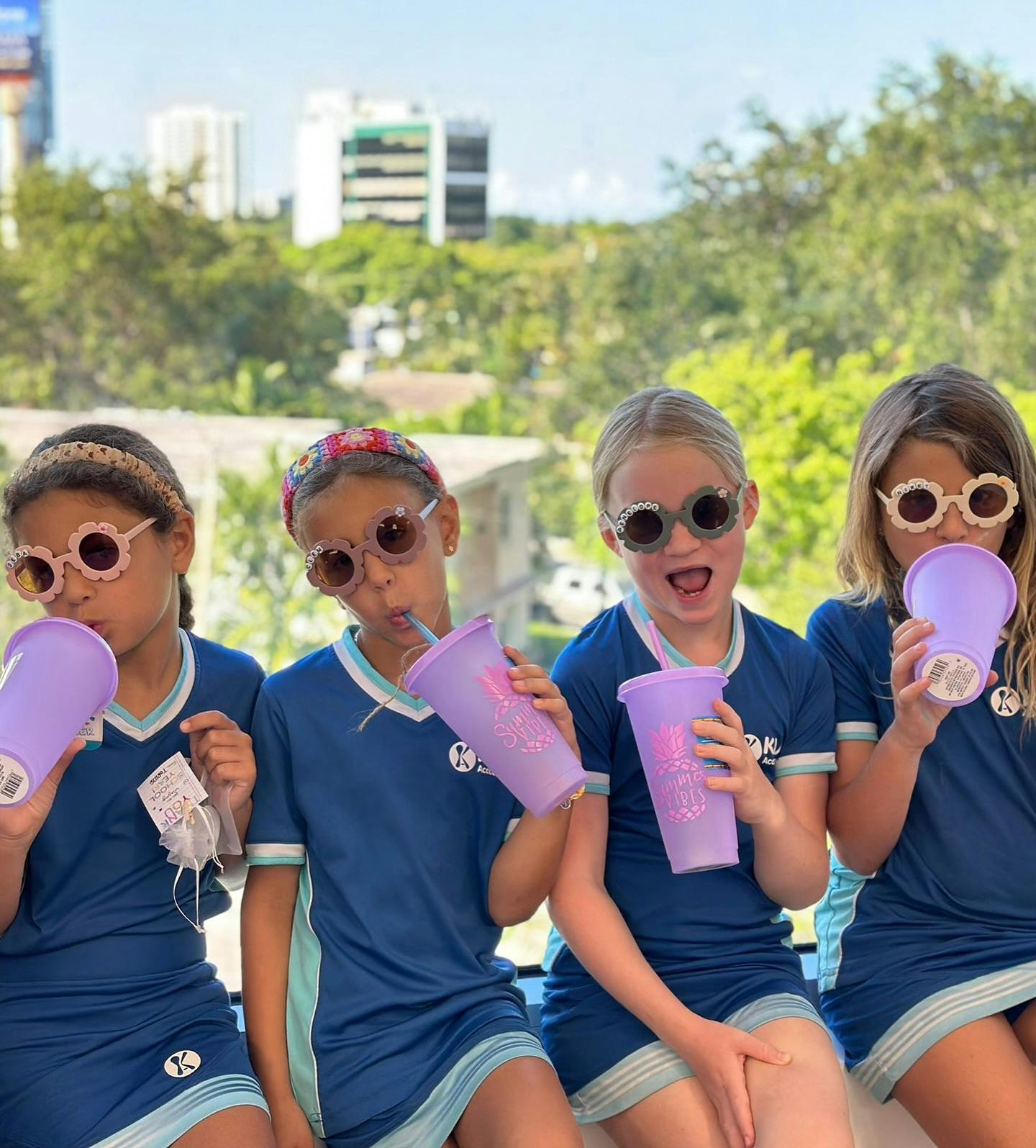 Four children in sunglasses holding purple cups