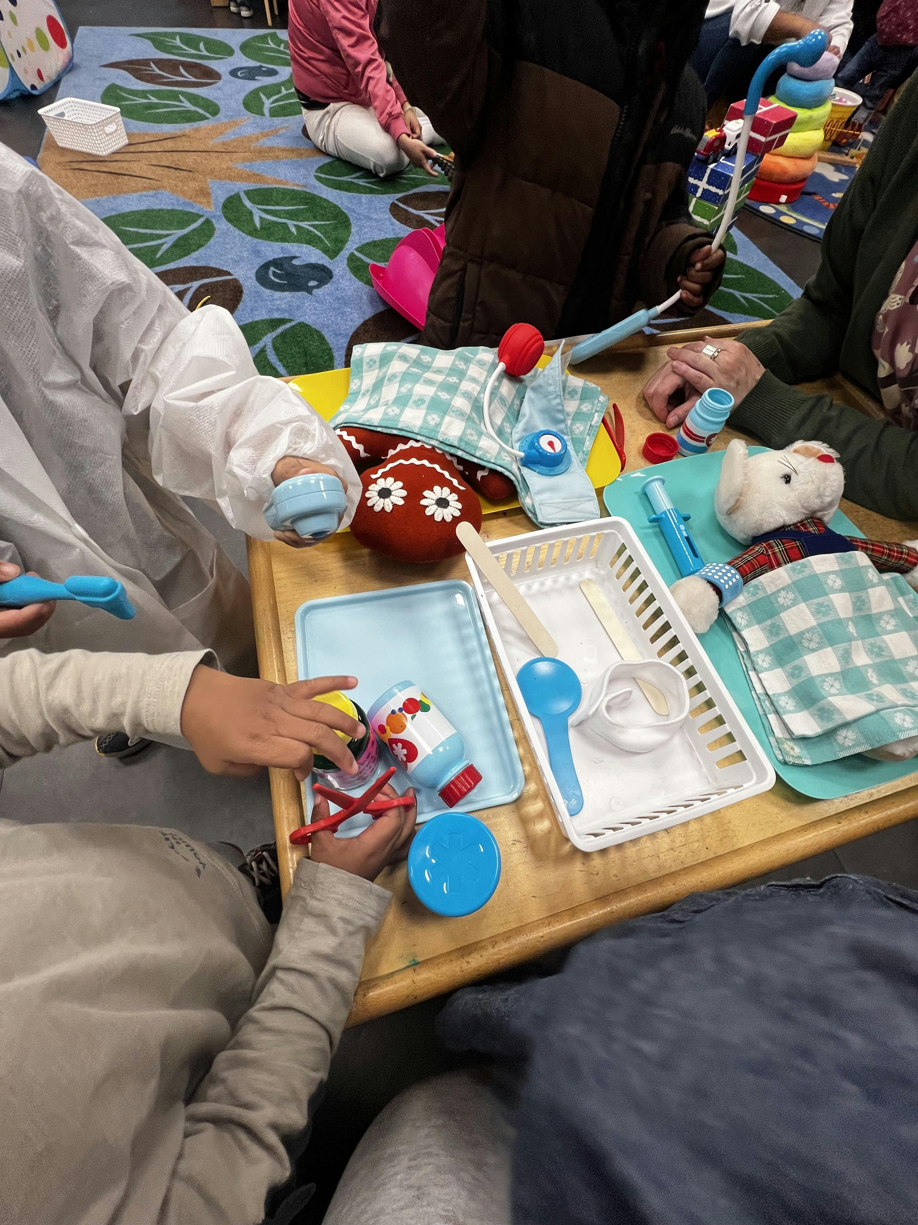 People playing with doctor's toys and stuffed animals on a wooden table