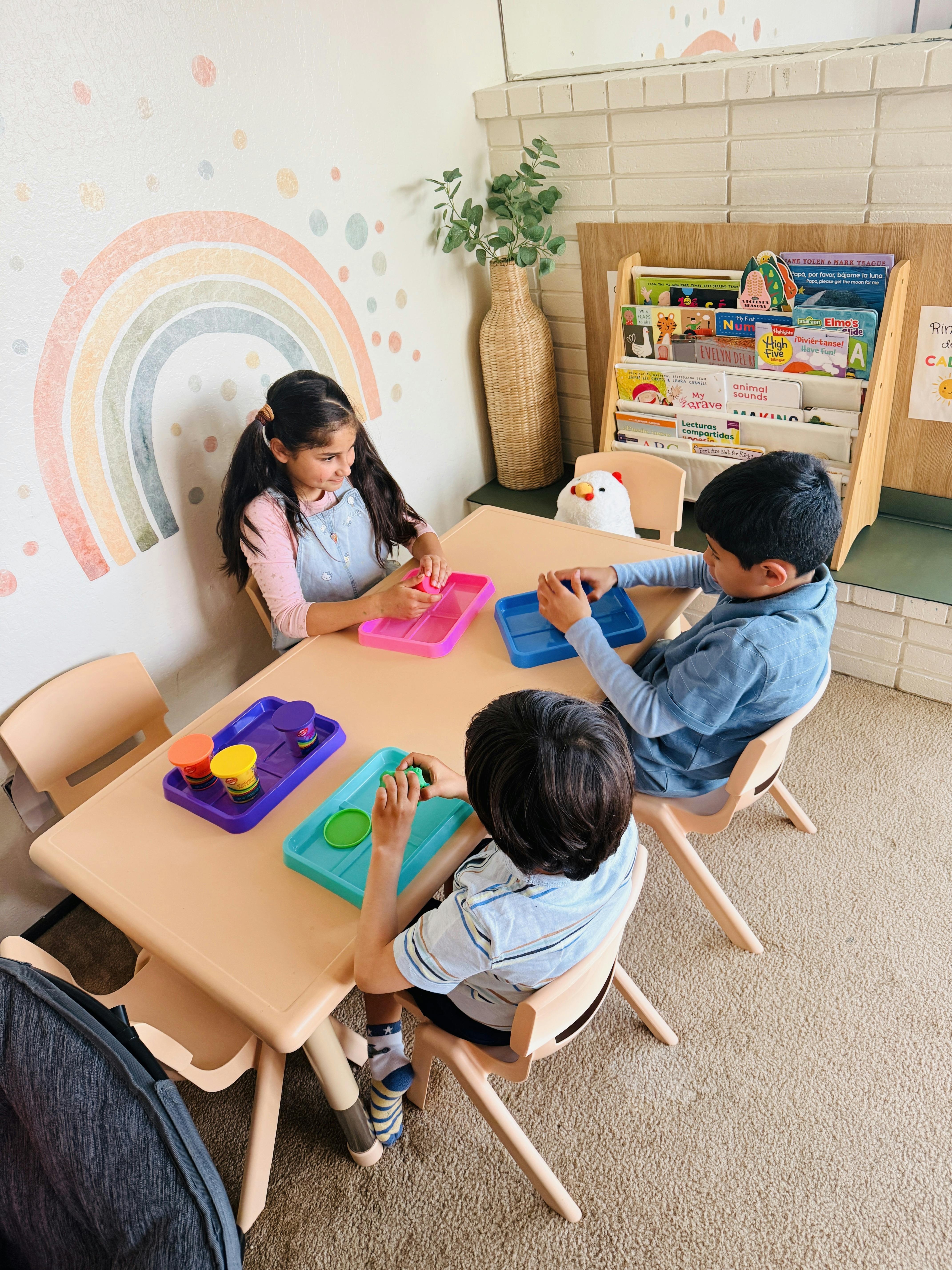 Three children playing with modeling clay at a table in a classroom
