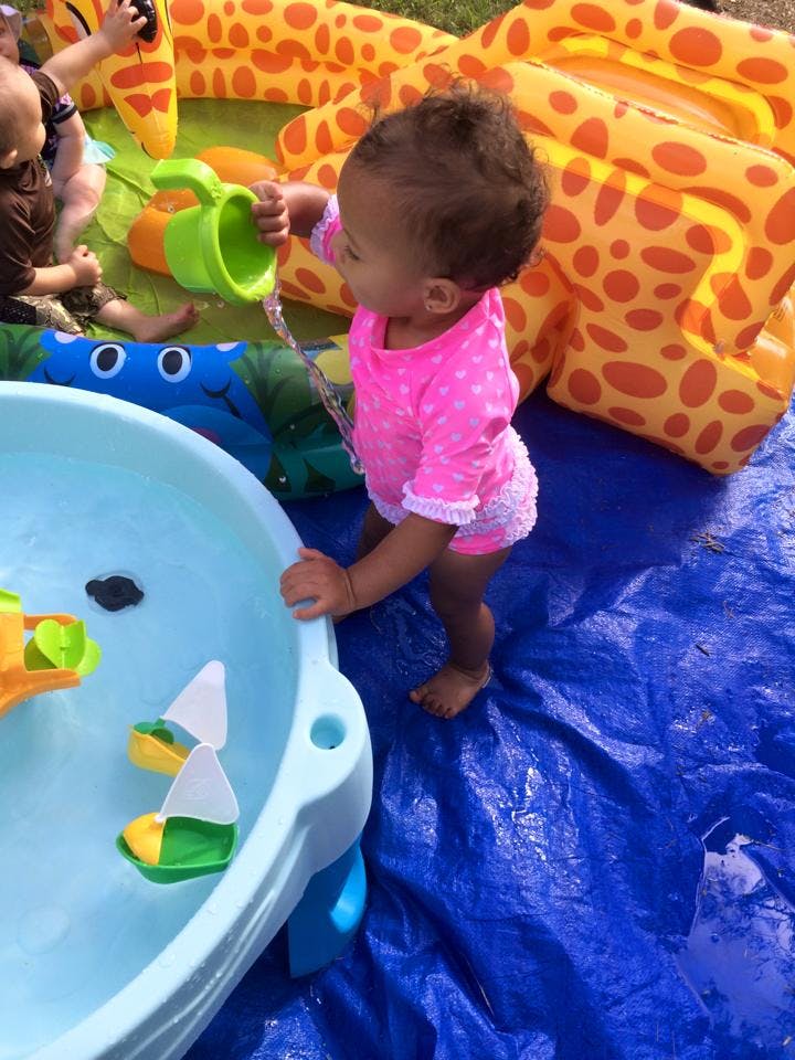 Child pouring water from a green toy into a water table