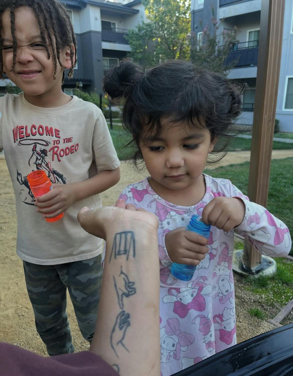Two children holding bottles, one with dreadlocks and a rodeo shirt
