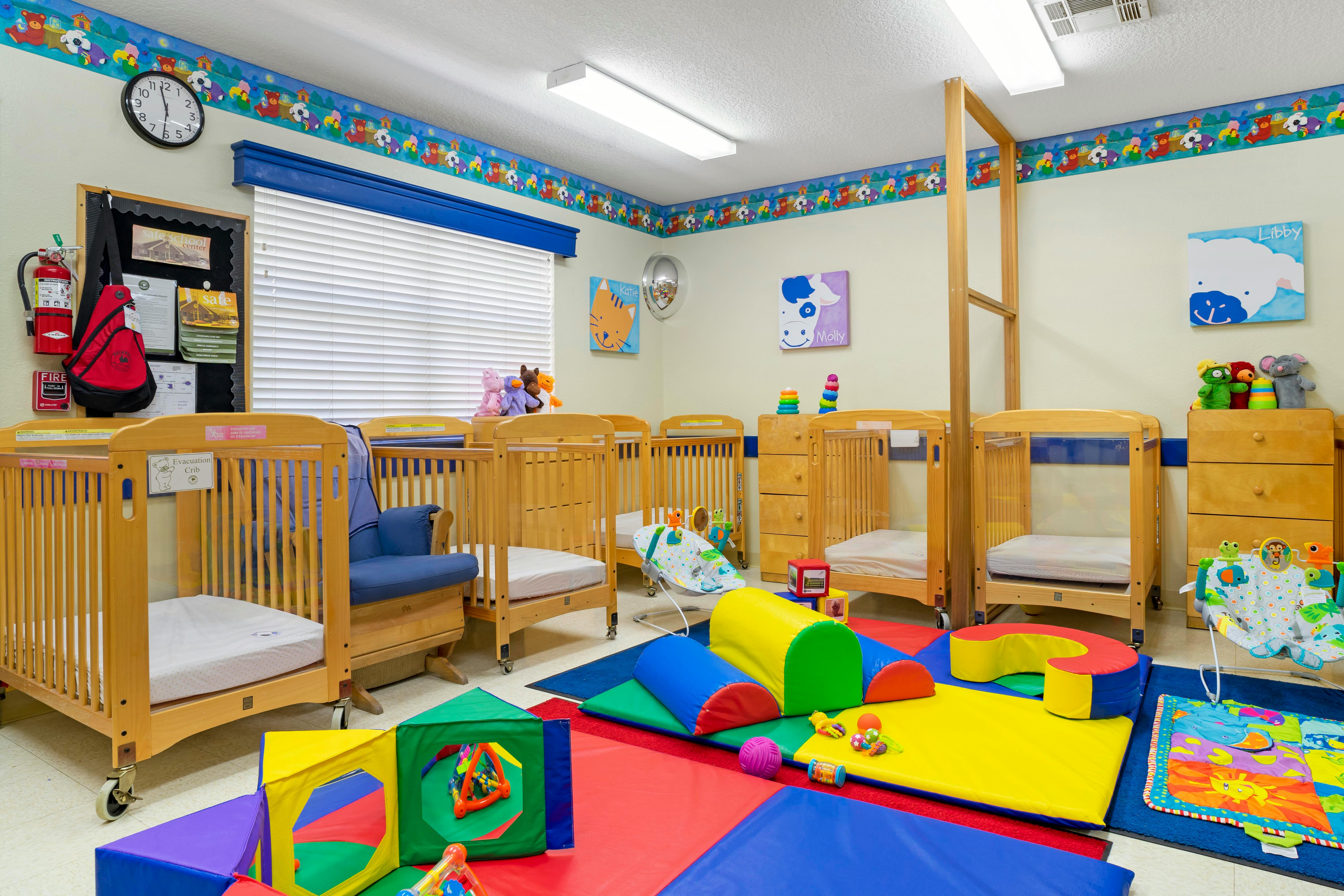 A room with multiple wooden cribs, a blue rocking chair, and colorful soft play equipment