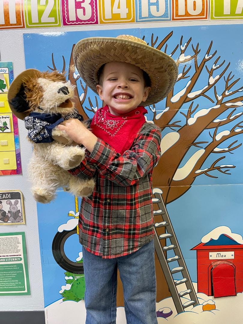 Child in a cowboy hat and plaid shirt holding a stuffed animal