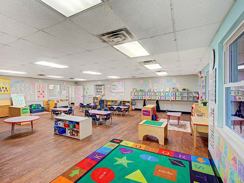 Spacious preschool classroom with small tables, chairs, and colorful rug