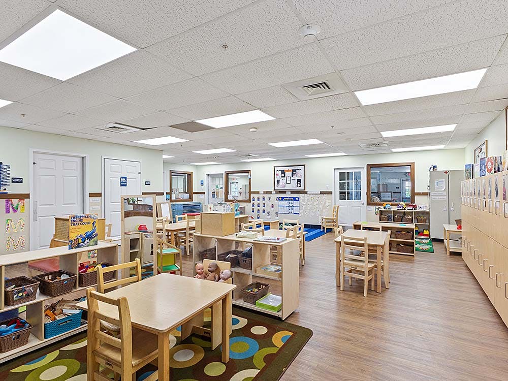 Empty classroom with small tables and chairs, shelves, and a colorful rug