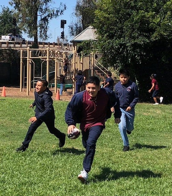 Three teens playing football on a grassy field, one carrying the ball