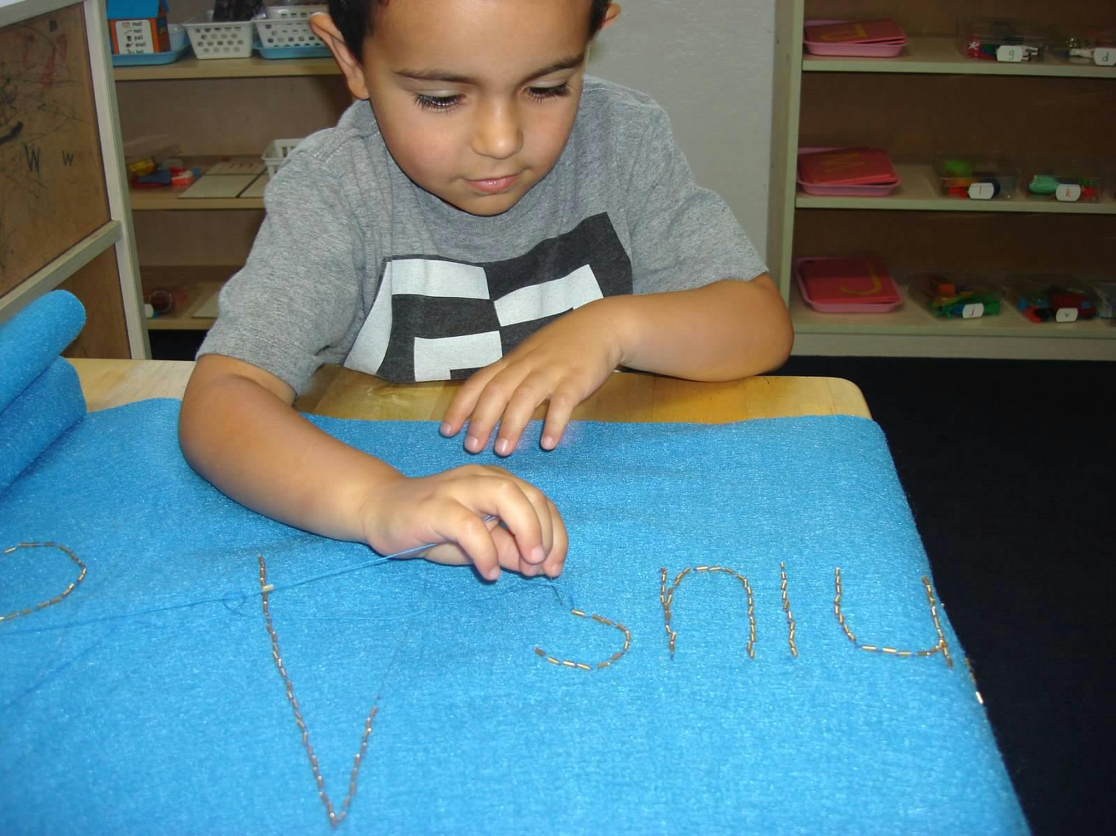 Child tracing letters on a blue mat