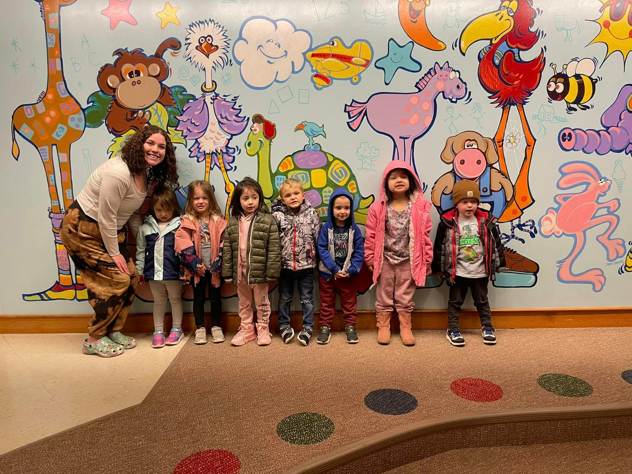 Adult and several children standing in front of a colorful mural