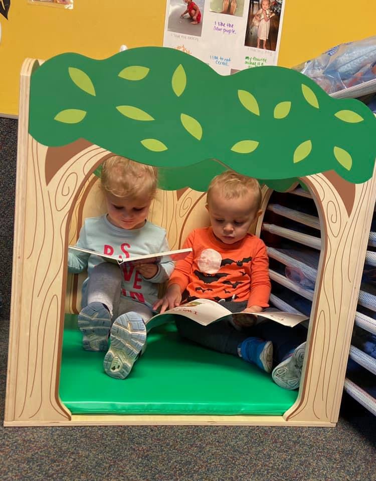 Two children reading books in a play structure shaped like a tree