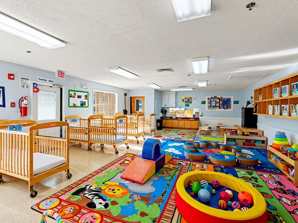 A colorful daycare room with cribs, play mats, and learning materials