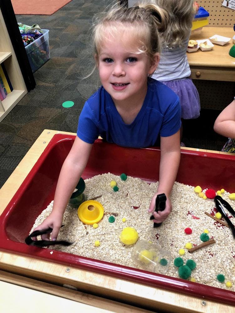 Child playing in a sensory bin with rice and small objects